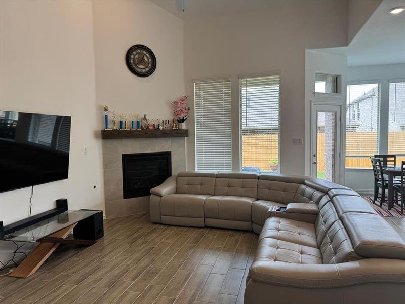 Spacious living area featuring high vaulted ceilings, light-tone tile flooring, and a corner fireplace with a wood mantel Spacious living area featuring high vaulted ceilings, light-tone tile flooring, and a corner fireplace with a wood mantel