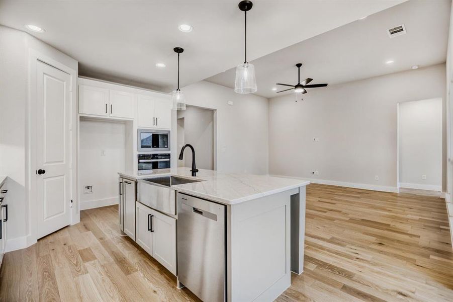 Kitchen with stainless steel appliances, white cabinetry, decorative light fixtures, and light wood-type flooring
