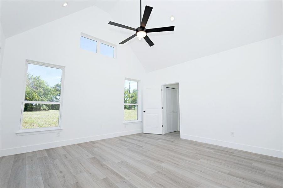 Empty room with high vaulted ceiling, plenty of natural light, light wood-style floors, a ceiling fan, and recessed lighting