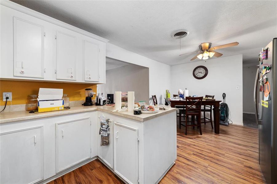Kitchen with light wood-type flooring, stainless steel fridge, kitchen peninsula, ceiling fan, and white cabinets