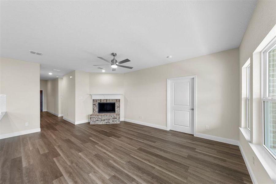 Spacious living area featuring wood-finish flooring, a brick fireplace with white mantel, a ceiling fan, recessed lighting, and multiple windows
