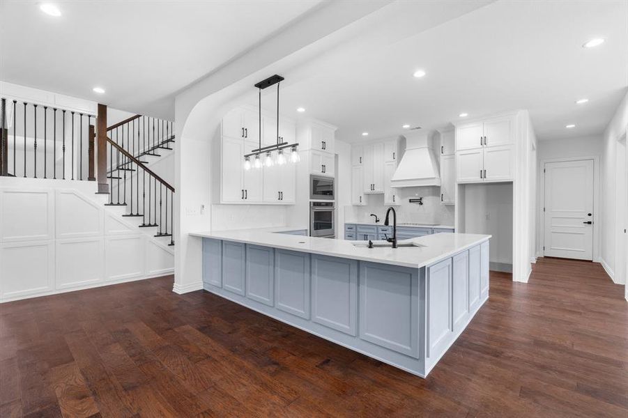 Kitchen featuring custom range hood, stainless steel appliances, light countertops, dark wood finished floors, and recessed lighting Kitchen featuring custom range hood, stainless steel appliances, light countertops, dark wood finished floors, and recessed lighting