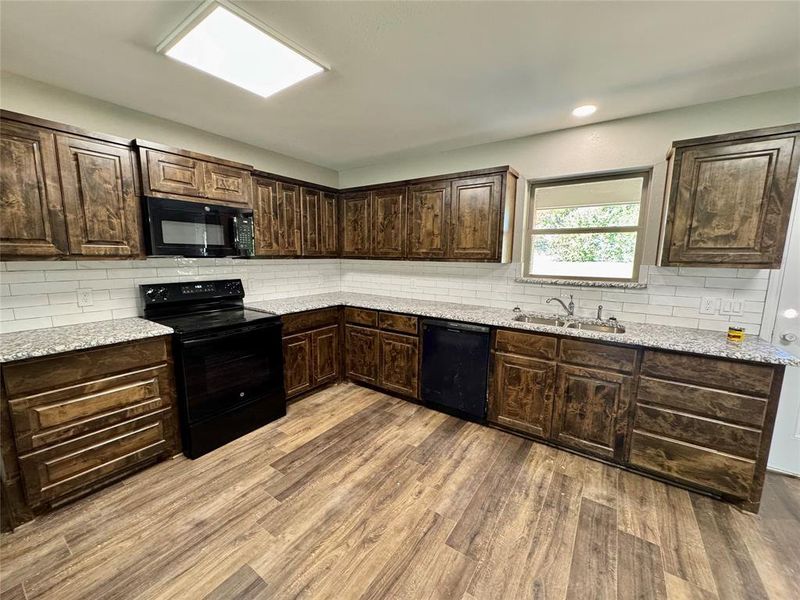 Kitchen featuring dark brown cabinets, backsplash, black appliances, light wood finished floors, and recessed lighting