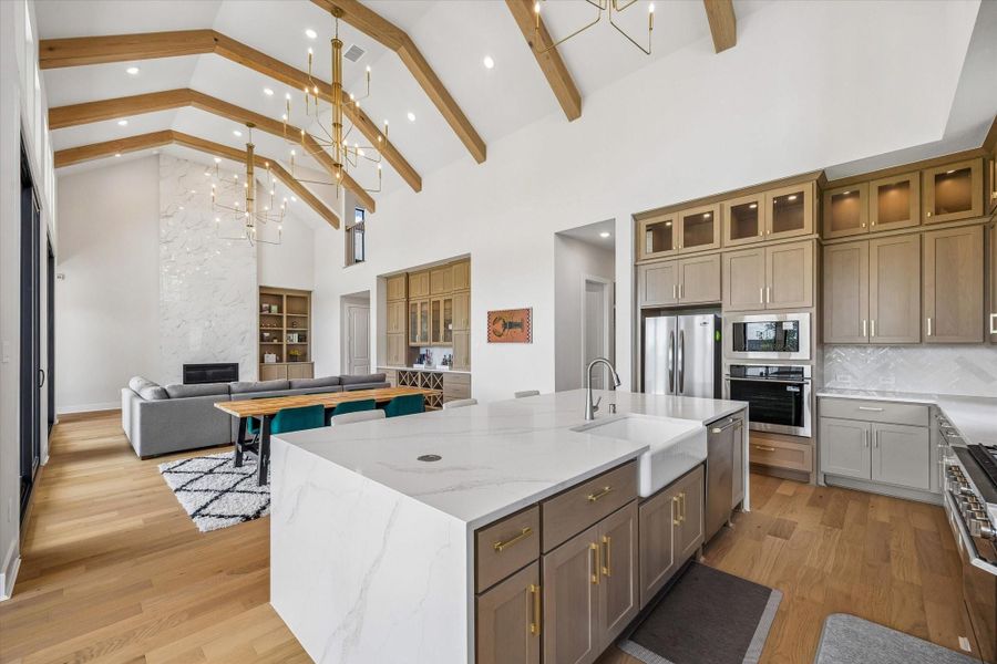 THE OPEN-CONCEPT KITCHEN FEATURES A LARGE WATERFALL ISLAND, FARMHOUSE SINK, QUARTZ COUNTERTOPS, EXTENSIVE CABINETRY, AND STAINLESS STEEL APPLIANCES. VAULTED CEILINGS WITH EXPOSED WOOD BEAMS CONTINUE INTO THE ADJOINING LIVING AREA. THE OPEN-CONCEPT KITCHEN FEATURES A LARGE WATERFALL ISLAND, FARMHOUSE SINK, QUARTZ COUNTERTOPS, EXTENSIVE CABINETRY, AND STAINLESS STEEL APPLIANCES. VAULTED CEILINGS WITH EXPOSED WOOD BEAMS CONTINUE INTO THE ADJOINING LIVING AREA.