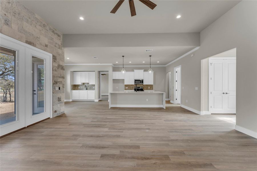 Unfurnished living room featuring ceiling fan, recessed lighting, ornamental molding, light wood-type flooring, and french doors