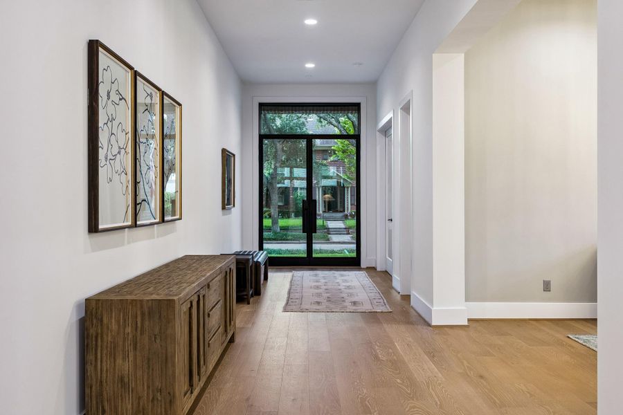 A view down the entry hall toward the glass front doors, showcasing the beautiful mature trees that surround the home.