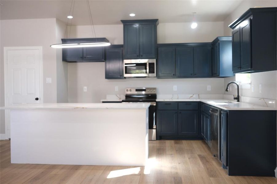 Kitchen with appliances with stainless steel finishes, decorative light fixtures, light wood-style flooring, and recessed lighting Kitchen with appliances with stainless steel finishes, decorative light fixtures, light wood-style flooring, and recessed lighting