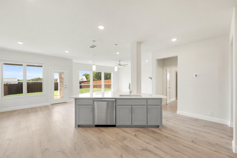 Kitchen island with gray cabinets, stainless dishwasher, and light wood floors in open-concept layout
