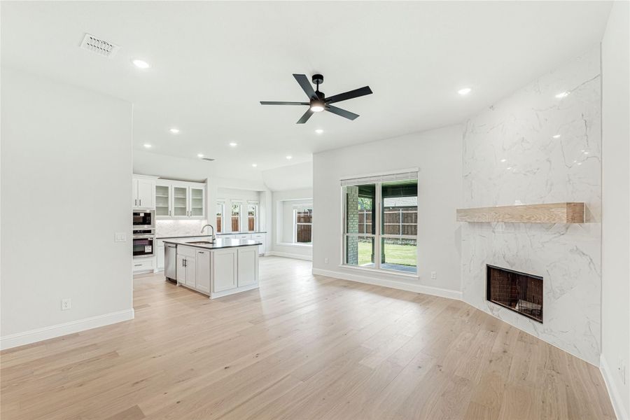 Open living area with marble fireplace, light hardwood floors, and kitchen island visible in background
