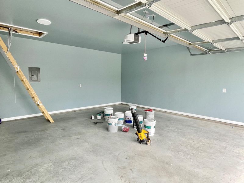 A spacious garage featuring a durable concrete floor and accessible attic storage.