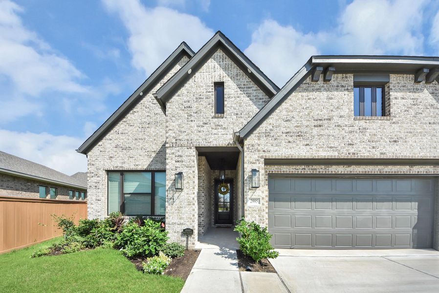 Charming modern home featuring a beautiful brick exterior, inviting entryway, and a spacious two-car garage, all set against a backdrop of lush landscaping.