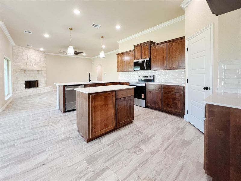 Kitchen with appliances with stainless steel finishes, crown molding, backsplash, a center island, and decorative light fixtures Kitchen with appliances with stainless steel finishes, crown molding, backsplash, a center island, and decorative light fixtures