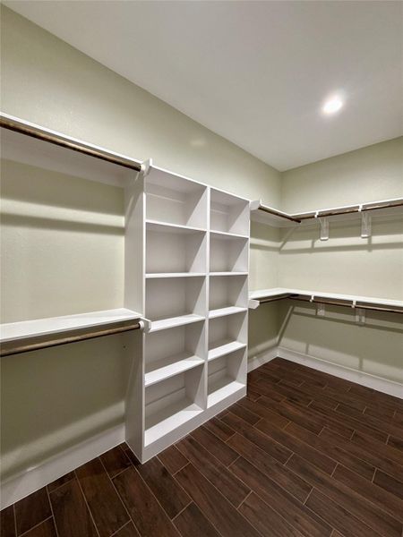 Spacious walk-in closet with ample shelving and hanging space, featuring dark wood look tile flooring and soft overhead lighting for a modern touch. Spacious walk-in closet with ample shelving and hanging space, featuring dark wood look tile flooring and soft overhead lighting for a modern touch.