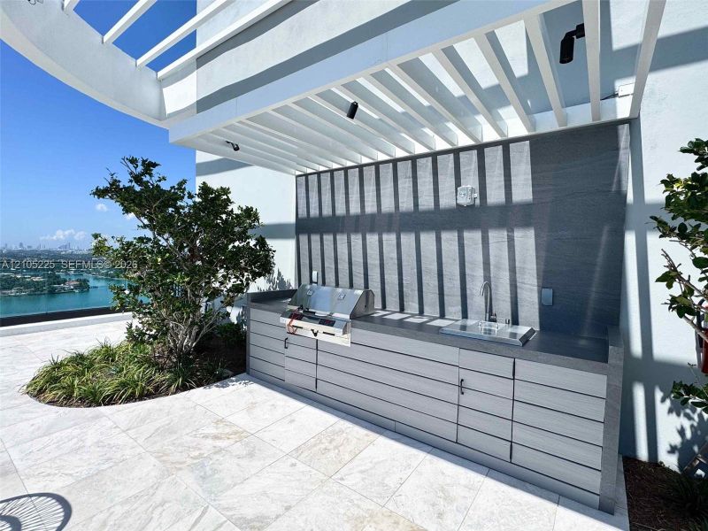 Outdoor kitchen featuring a built-in grill, integrated sink, and cabinetry