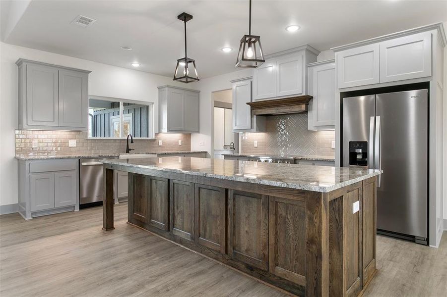 Kitchen featuring appliances with stainless steel finishes, light hardwood / wood-style floors, a kitchen island, and light stone counters