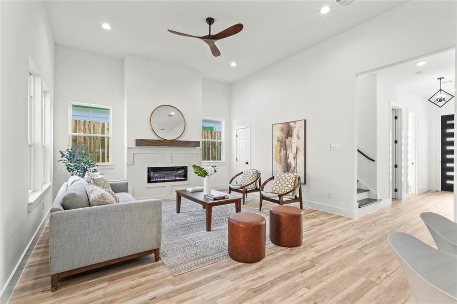 Living area with light wood finished floors, a ceiling fan, recessed lighting, a glass covered fireplace, and stairs