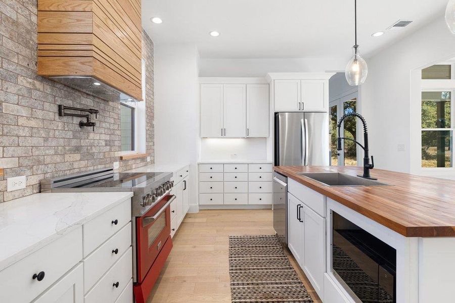 Kitchen with stainless steel appliances, white cabinetry, and wooden counters
