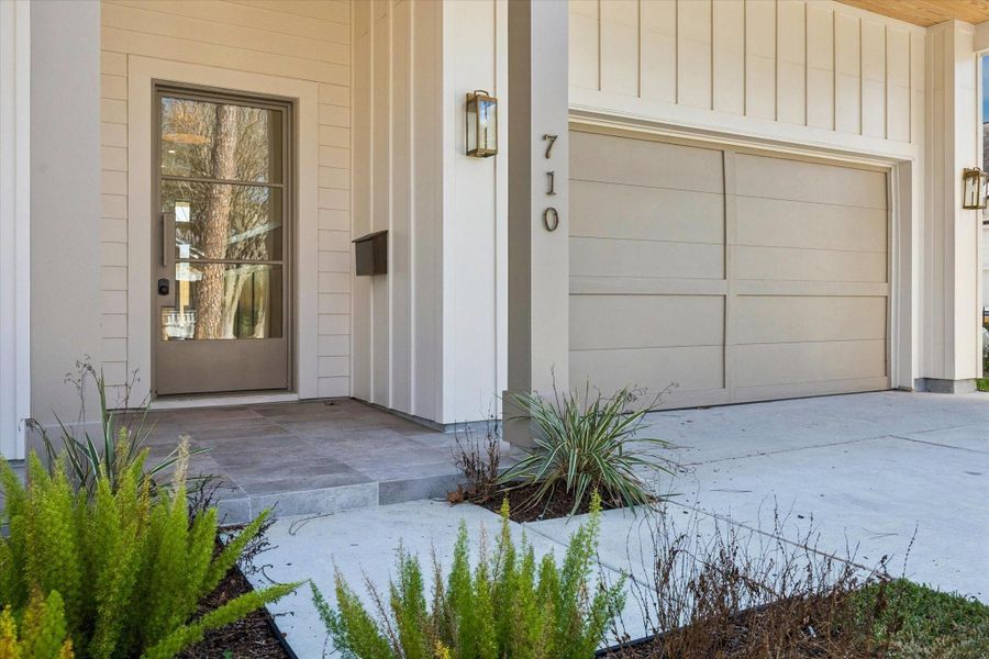 The home’s exterior features custom antique brass house numbers, a neutral color palette, and a beautifully landscaped yard, highlighted by a substantial metal grid-style glass front door.