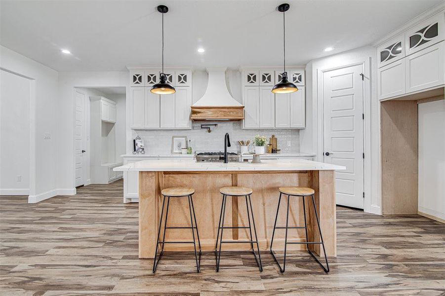 Kitchen with white cabinets, pendant lighting, custom range hood, and an island with sink