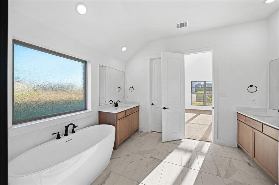 Full bath featuring a freestanding bath, recessed lighting, two vanities, light marble finish floors, and vaulted ceiling Full bath featuring a freestanding bath, recessed lighting, two vanities, light marble finish floors, and vaulted ceiling