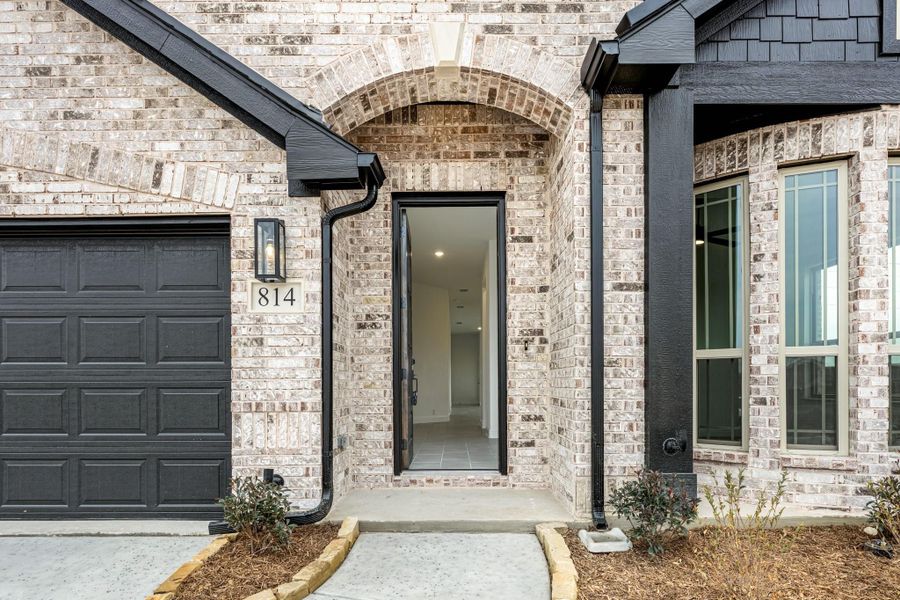 Brick home entrance with arched doorway, black front door, and single-car garage at address 814