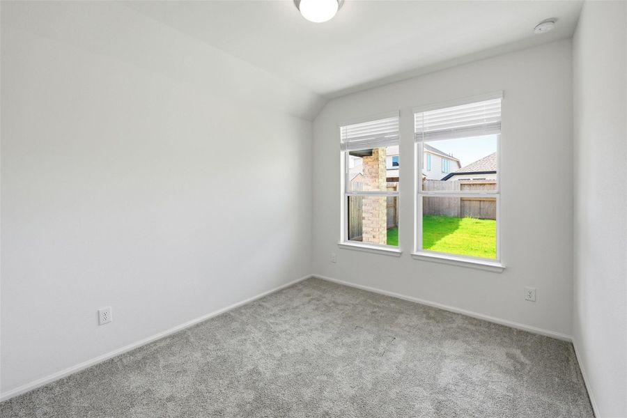 Bright and cozy room with plush carpeting, neutral walls, and large windows offering a view of the lush backyard.