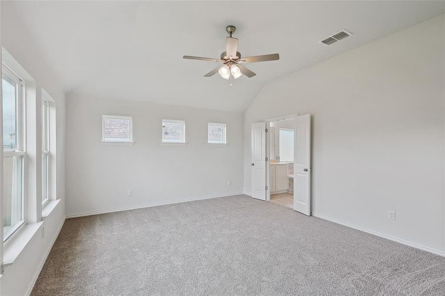 Spare room featuring light carpet, vaulted ceiling, ceiling fan, and a healthy amount of sunlight