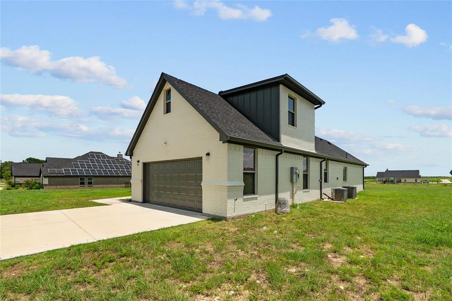 View of side of home with board and batten siding, driveway, brick siding, a yard, and an attached garage View of side of home with board and batten siding, driveway, brick siding, a yard, and an attached garage
