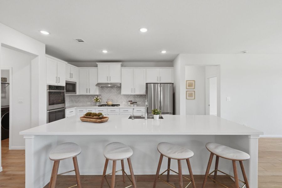 Modern kitchen with a spacious island, white cabinetry, stainless steel appliances, and recessed lighting. Ideal for entertaining and meal prep.