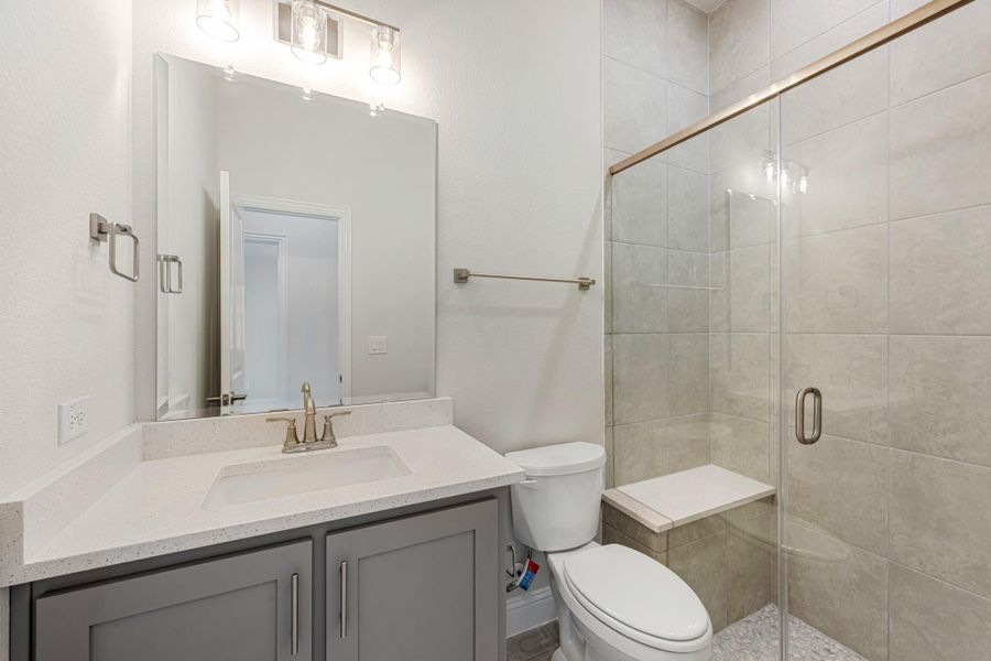 Bathroom with gray vanity, white countertop, and glass-enclosed tile shower with bench seat Bathroom with gray vanity, white countertop, and glass-enclosed tile shower with bench seat