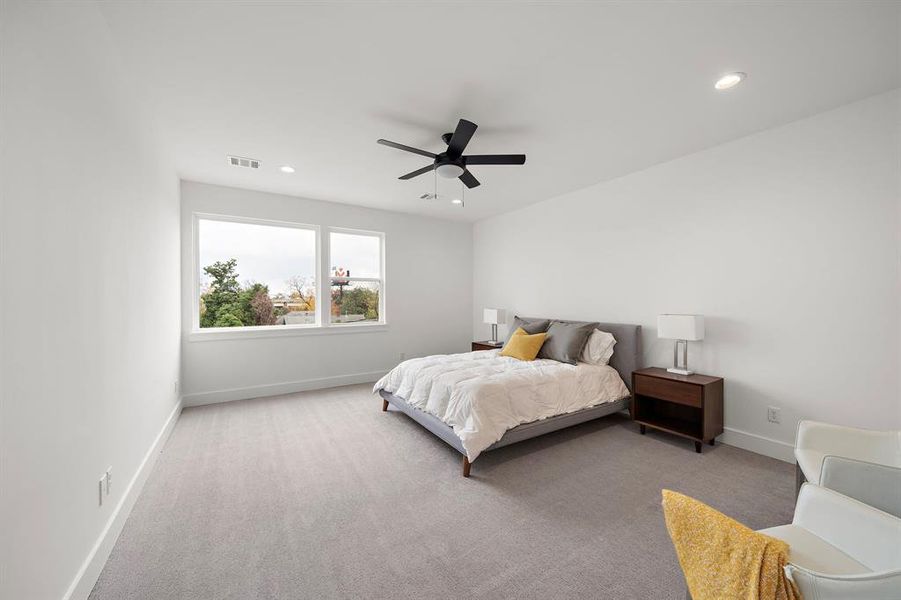 This spacious owner's bedroom is bathed in natural light, creating a bright and serene retreat. Large windows highlight the elegant design, offering a perfect space for relaxation and rest.