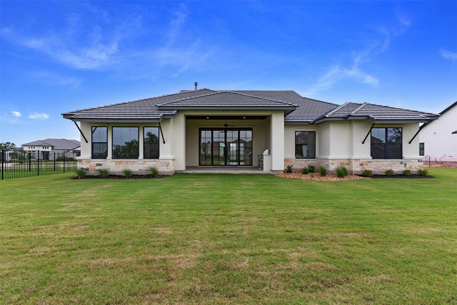 Expansive green lawn surrounds a sophisticated stucco and stone home with a generous covered patio.