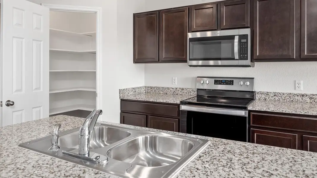 Kitchen with stainless steel appliances, dark wood finish cabinets, and light stone counters