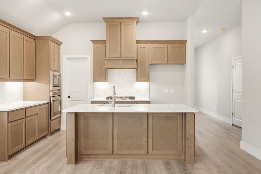 Kitchen with light wood cabinets, large center island, white countertops, and herringbone tile backsplash Kitchen with light wood cabinets, large center island, white countertops, and herringbone tile backsplash