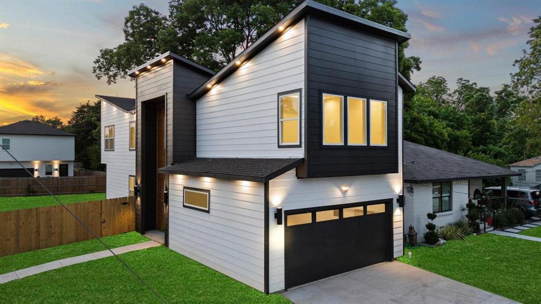 Contemporary house featuring an attached garage, a shingled roof, driveway, and brick siding