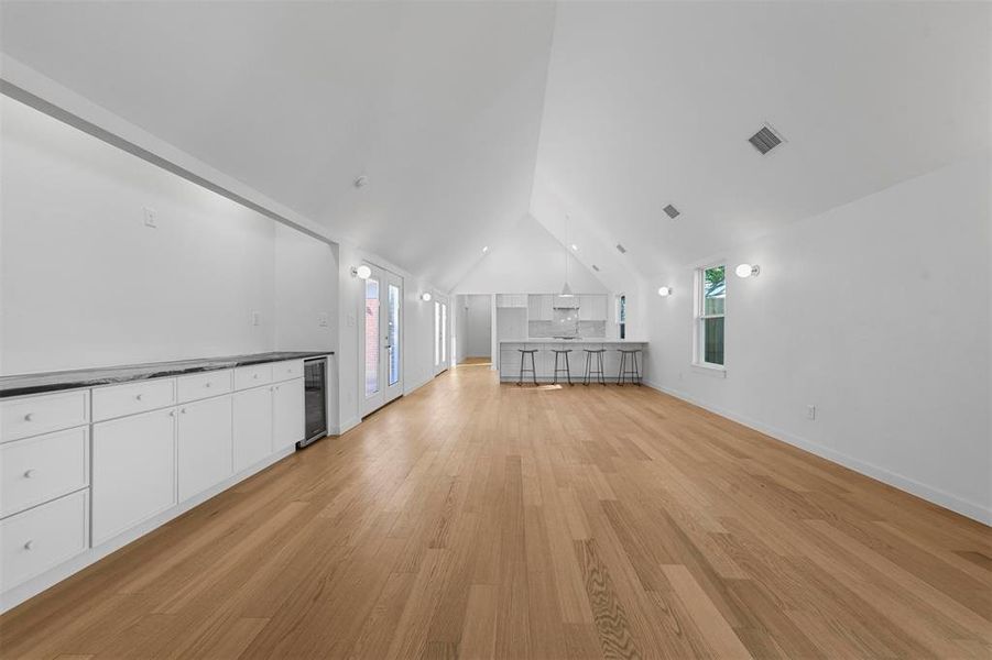 Unfurnished living room with lofted ceiling, light hardwood / wood-style floors, and wine cooler