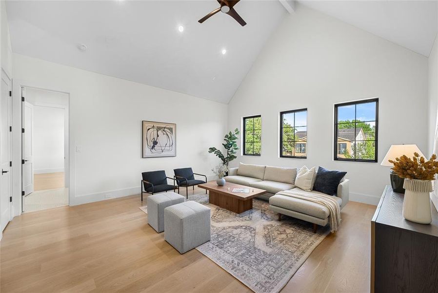Vaulted ceiling living area featuring light wood-finish flooring, recessed lighting, and three black-framed windows