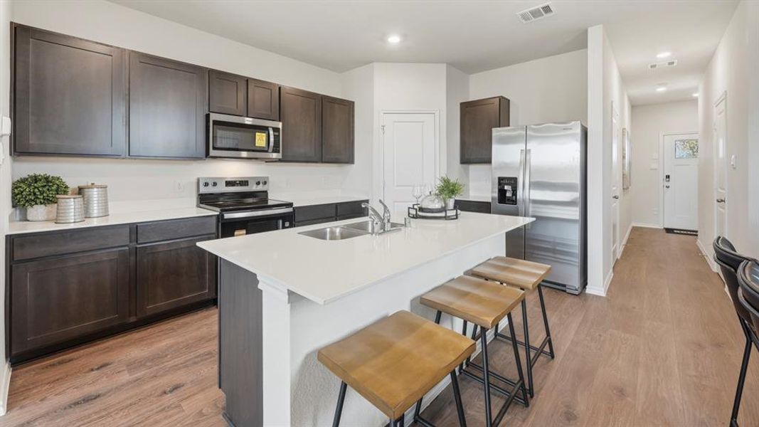 Kitchen featuring appliances with stainless steel finishes, a breakfast bar, light wood finished floors, an island with sink, and dark brown cabinets