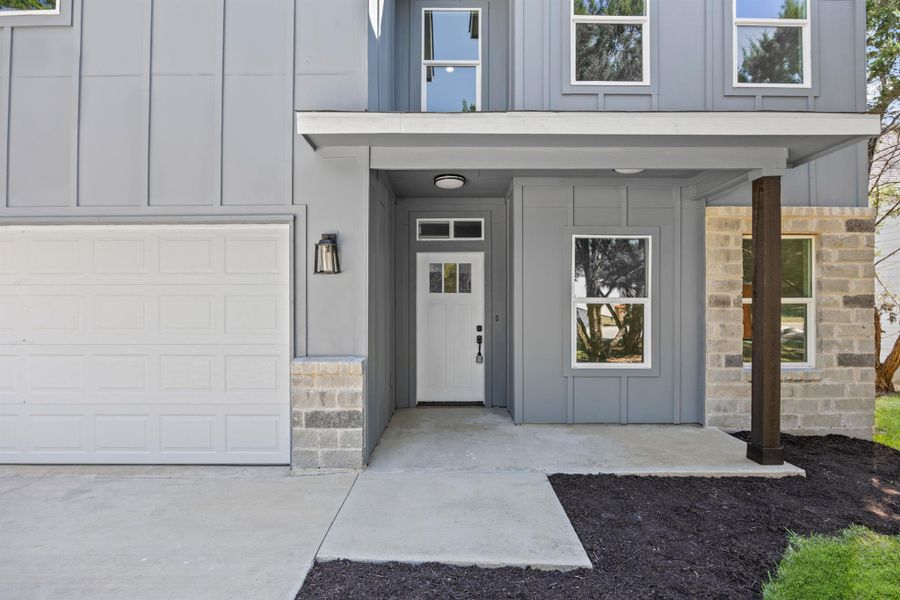 View of exterior entry with board and batten siding, a garage, stone siding, and a porch View of exterior entry with board and batten siding, a garage, stone siding, and a porch