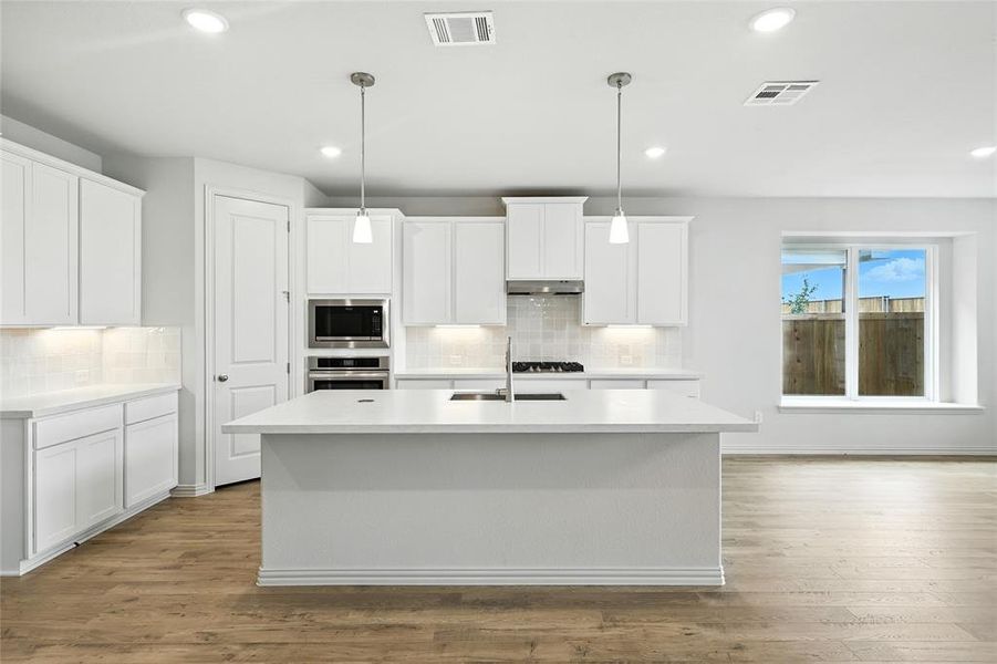 Kitchen with white cabinetry, tasteful backsplash, a center island with sink, and recessed lighting