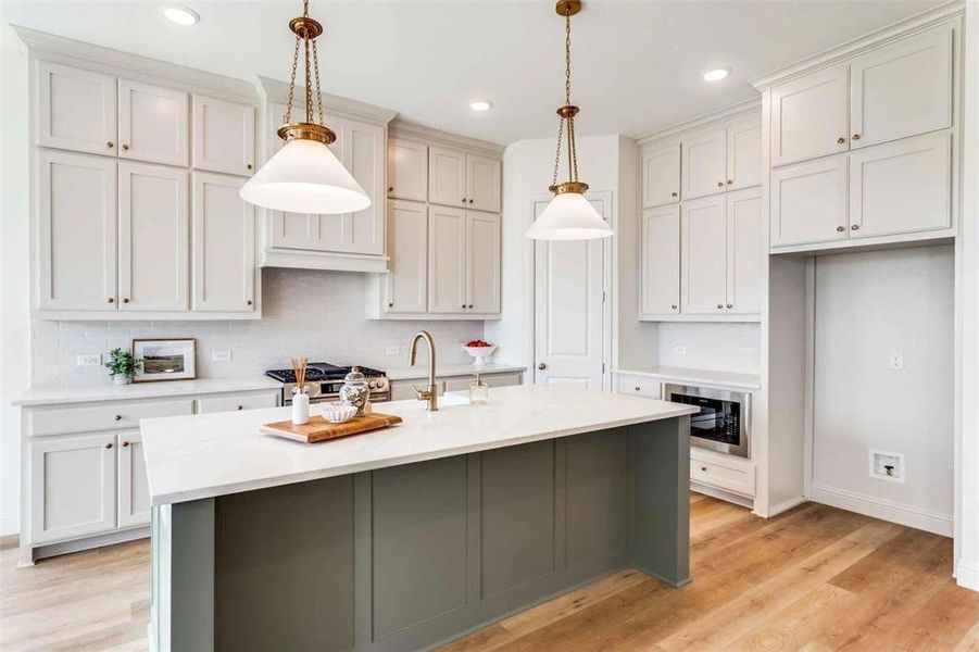 Kitchen with light wood-style flooring, decorative backsplash, hanging light fixtures, a kitchen island with sink, and white cabinetry Kitchen with light wood-style flooring, decorative backsplash, hanging light fixtures, a kitchen island with sink, and white cabinetry
