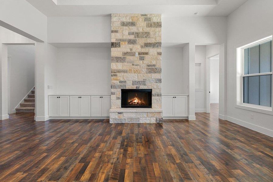Unfurnished living room with a stone fireplace, a high ceiling, and dark wood finished floors