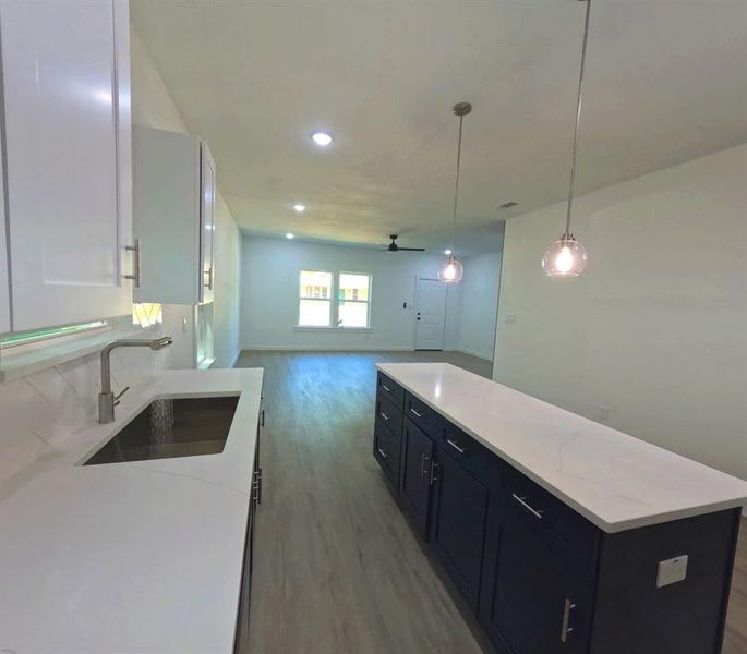 Kitchen featuring decorative light fixtures, a center island, dark wood-style floors, light stone counters, and open floor plan Kitchen featuring decorative light fixtures, a center island, dark wood-style floors, light stone counters, and open floor plan