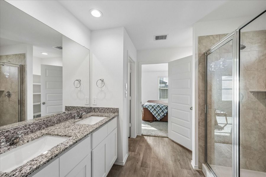 Primary bathroom with dual sinks, granite countertops, and a large mirror. The space features a glass-enclosed shower and wood-look flooring.