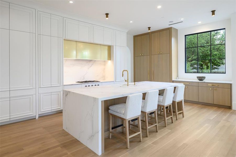 Kitchen with a breakfast bar area, light stone countertops, light wood-style floors, white cabinets, and recessed lighting Kitchen with a breakfast bar area, light stone countertops, light wood-style floors, white cabinets, and recessed lighting