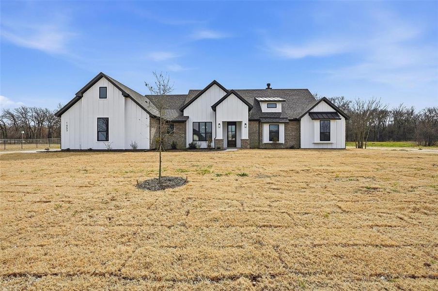 Modern farmhouse featuring board and batten siding, a front lawn, and roof with shingles