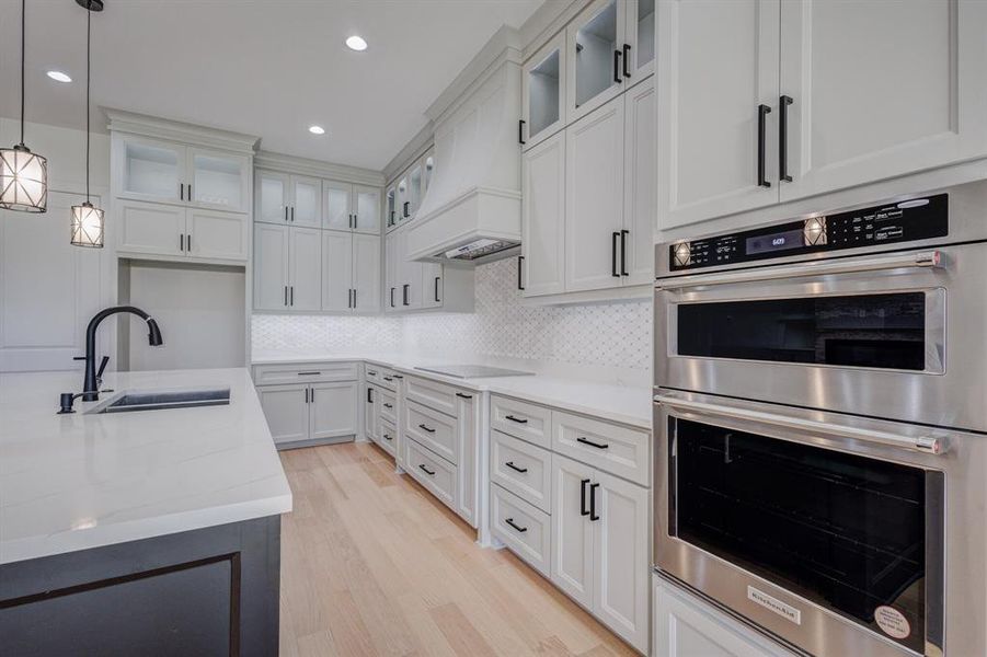 Kitchen featuring light wood-finish flooring, white perimeter cabinetry with black hardware, white quartz countertops, and a white geometric tile backsplash Kitchen featuring light wood-finish flooring, white perimeter cabinetry with black hardware, white quartz countertops, and a white geometric tile backsplash