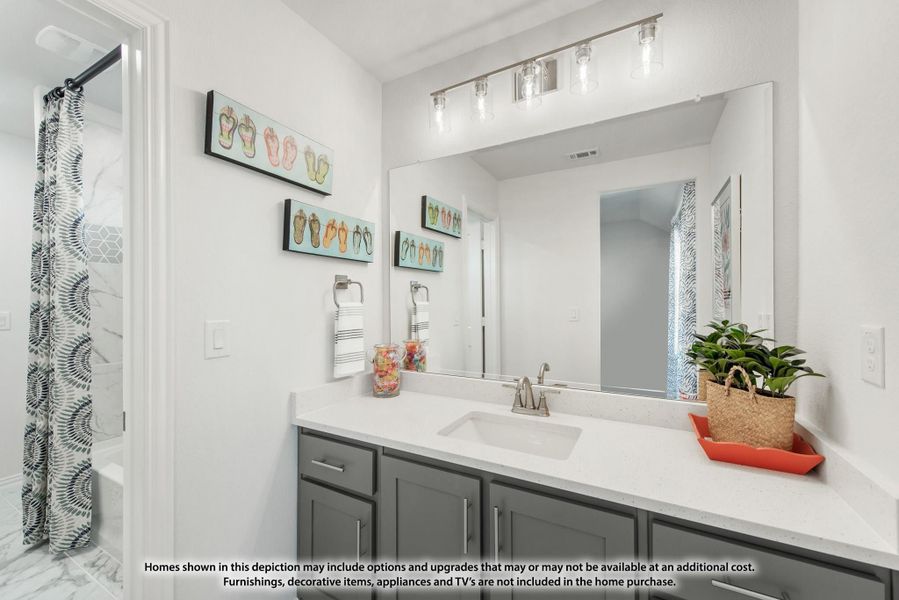 Bathroom with gray vanity, white countertop, large mirror, and shower with patterned curtain visible through doorway Bathroom with gray vanity, white countertop, large mirror, and shower with patterned curtain visible through doorway