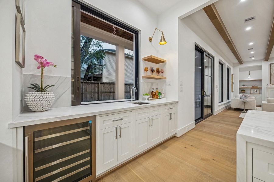 Fantastic Wet-Bar with a Sliding Glass Window! Pass drinks and food back and forth to the outside Bar/Grill Area. There are Inset Soft-Close Shaker Style Cabinets/Drawers with a Slab Quartz Counter and Backsplash, Kraus 17" Undermount Single Basin Stainless Steel Sink with Brizo Bar Faucet, White Oak Floating Shelves with a Natural Stain, Iron Swing Arm Sconce in a Brass Gold Finish. There is also a Zephyr Dual Zone Wine Cooler.