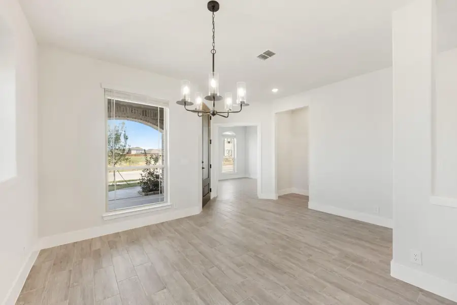 Empty dining room with light wood floors, white walls, chandelier, and large window with outdoor view